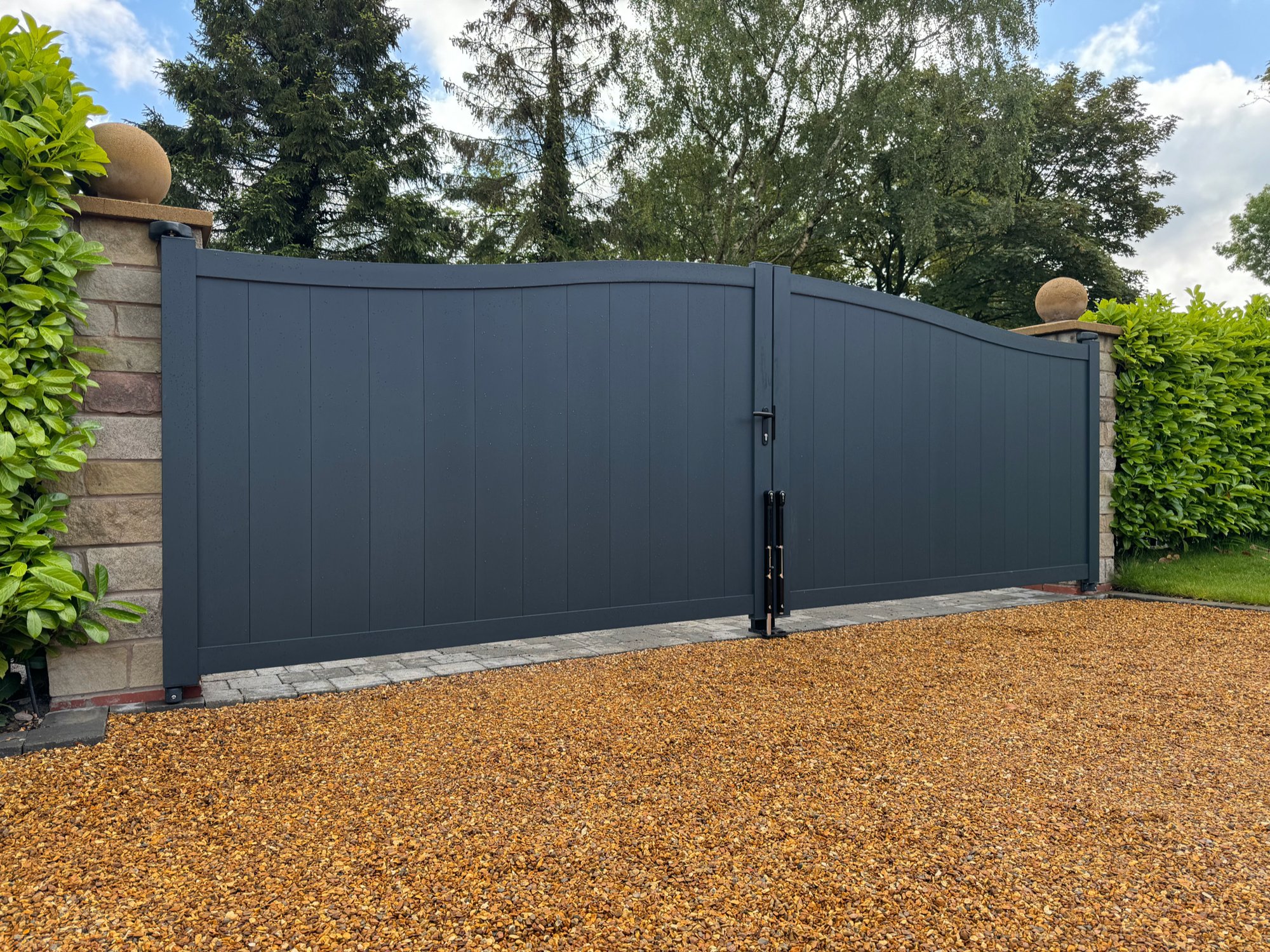 Grey aluminium double entrance gates installed by Tatton Fencing between stone pillars